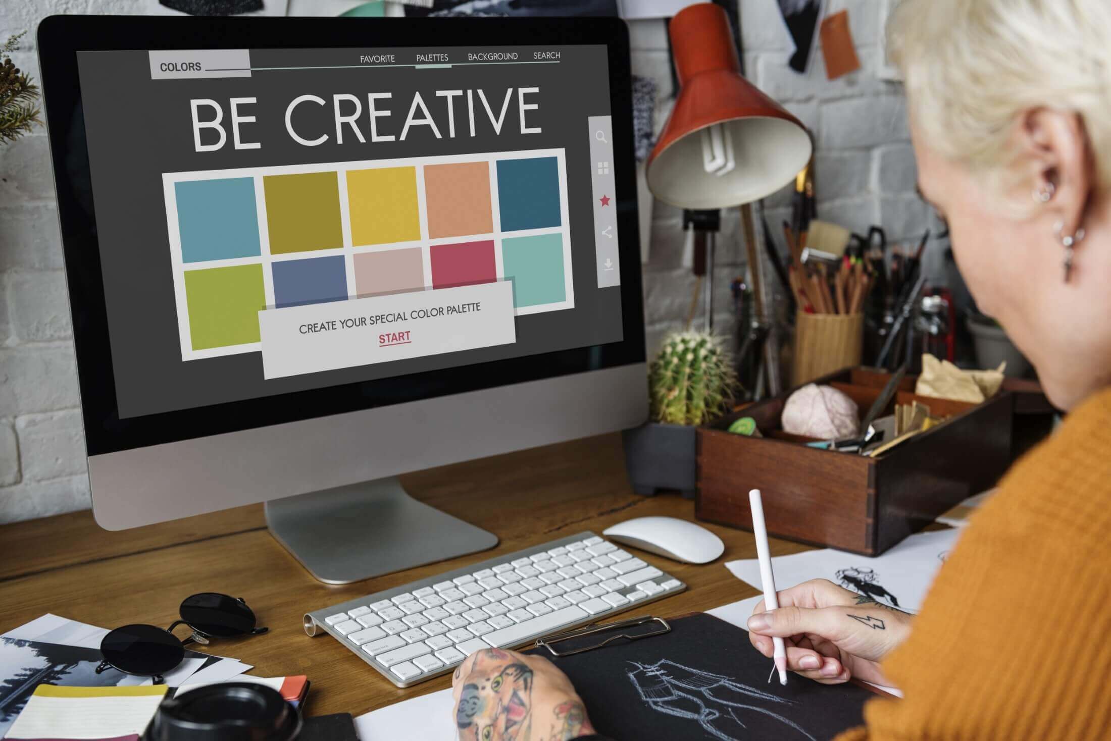 An image showcasing a computer screen with a colorful CMYK graphic, with a person holding a stylus, suggesting a creative design process taking place.