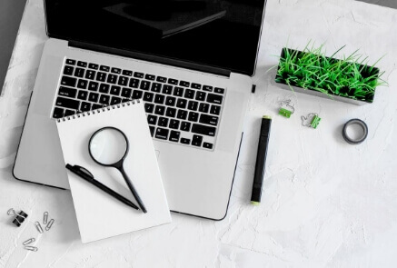 Magnifying glass and pen above laptop