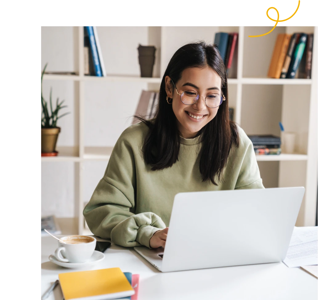 Attractive happy young girl student studying at the college library, sitting at the desk, using laptop computer