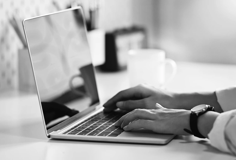 Close-up of hands typing on a laptop in black and white