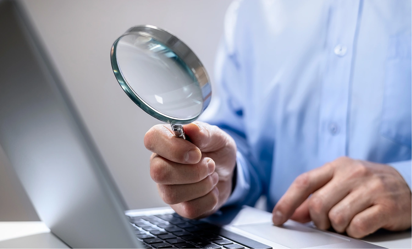Person holding a magnifying glass while using a laptop