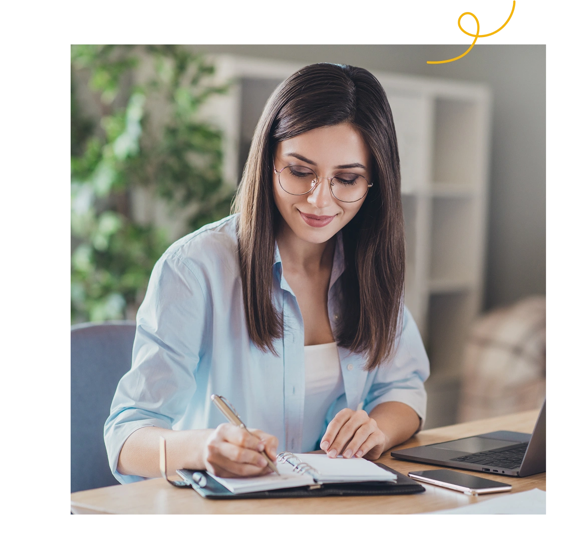 Woman writing in a notebook while working at a laptop
